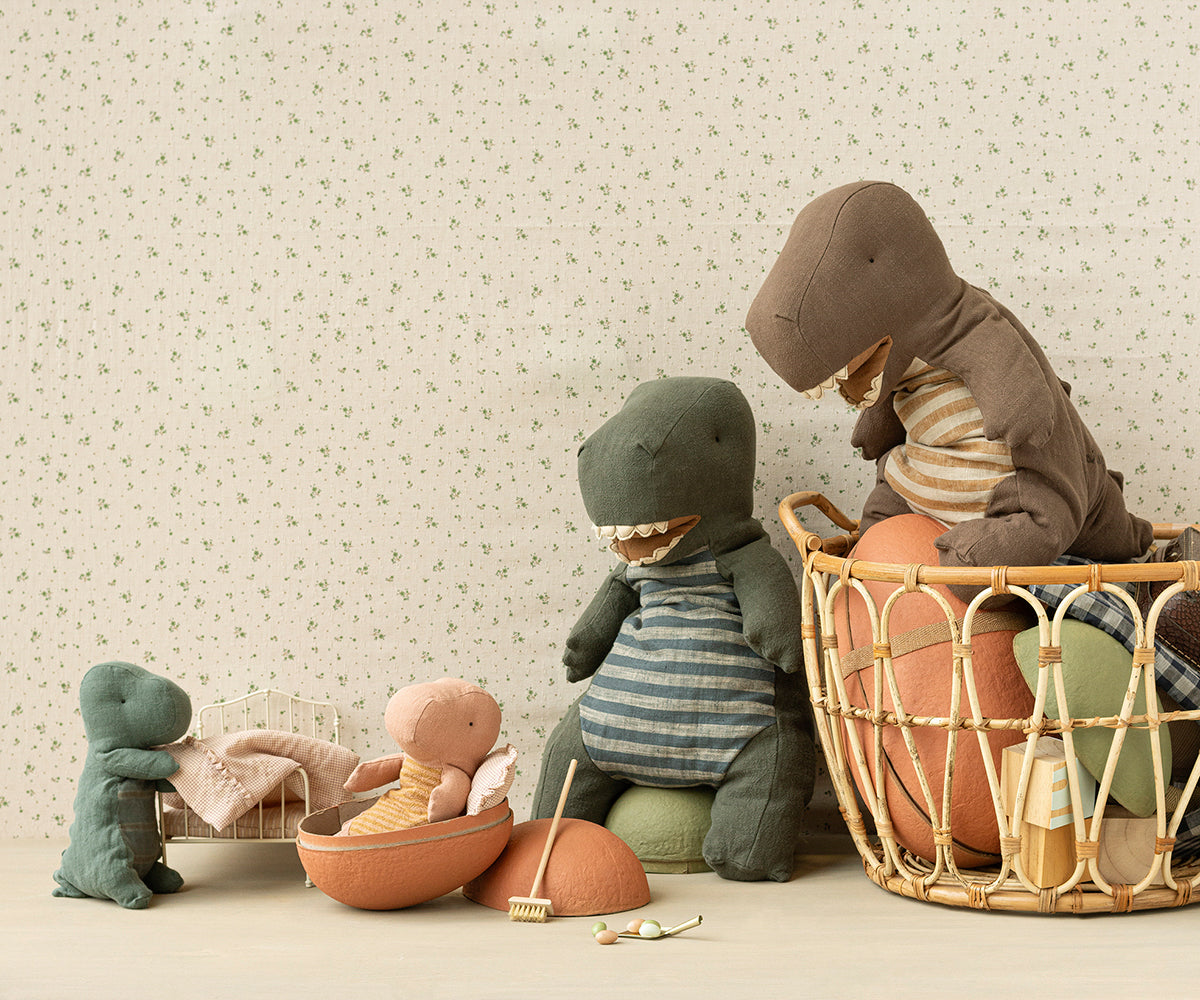 Children's toys, including a dinosaur and teddy bear, in a basket against a floral-patterned wall.