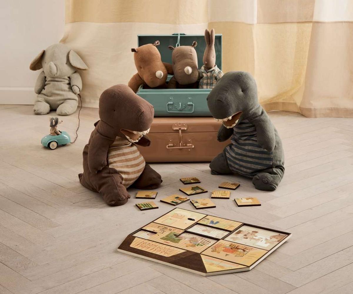 Stuffed animal toys playing with a suitcase and cards on a wooden floor.