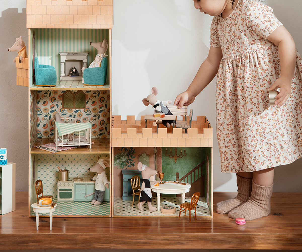 Child playing with a dollhouse filled with miniature furniture and accessories.