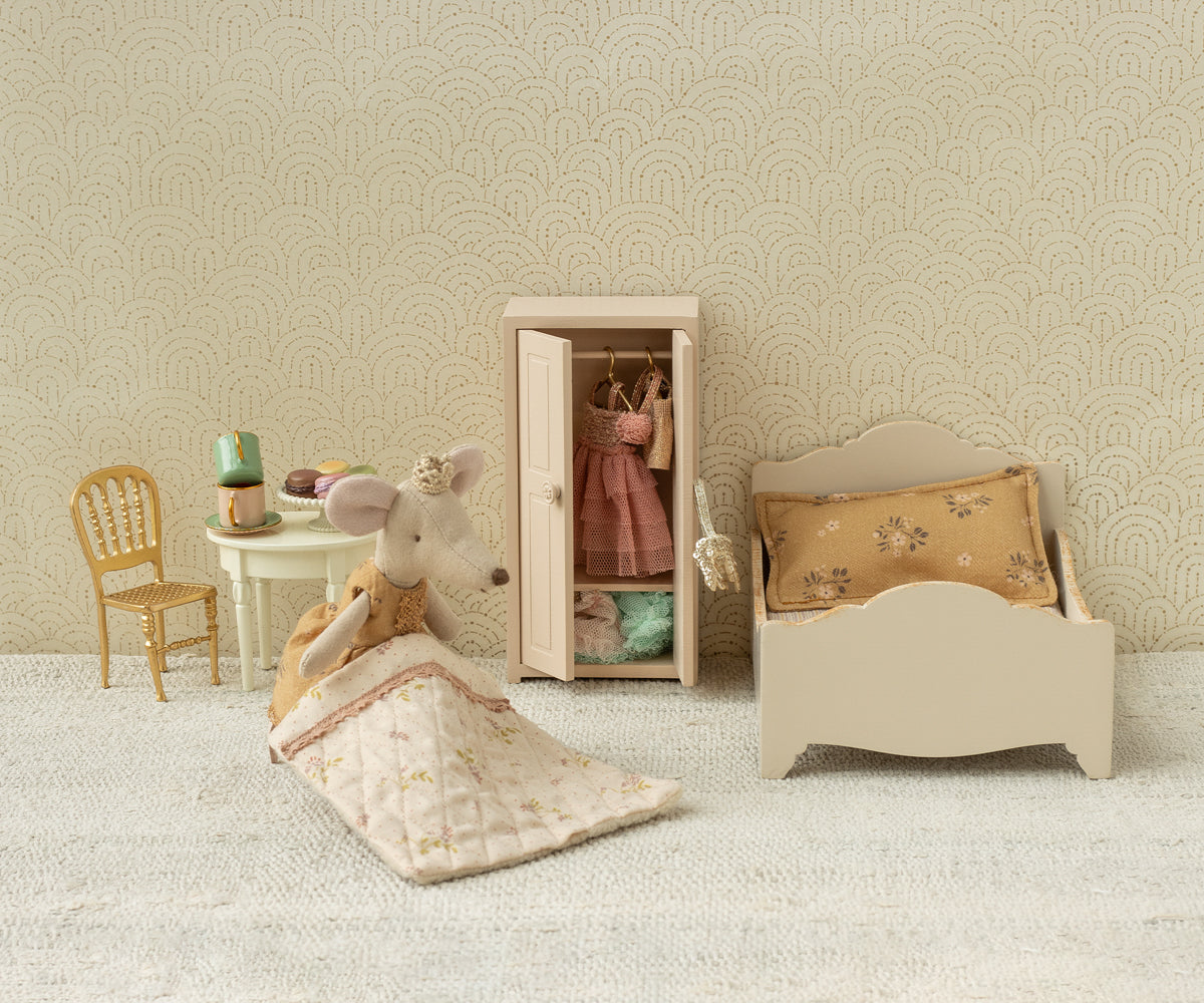 Miniature bedroom set with bed, wardrobe, chair, and mouse figure on a textured surface.