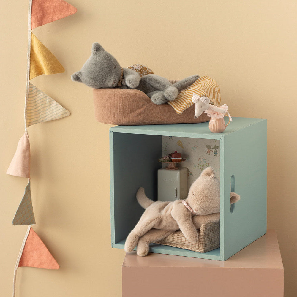 Children's room with a teal cube, plush toys, and decorative pillows on a beige wall.