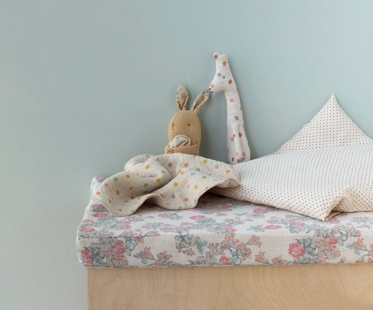 Children's bed with floral bedding, plush toys, and a light blue wall.