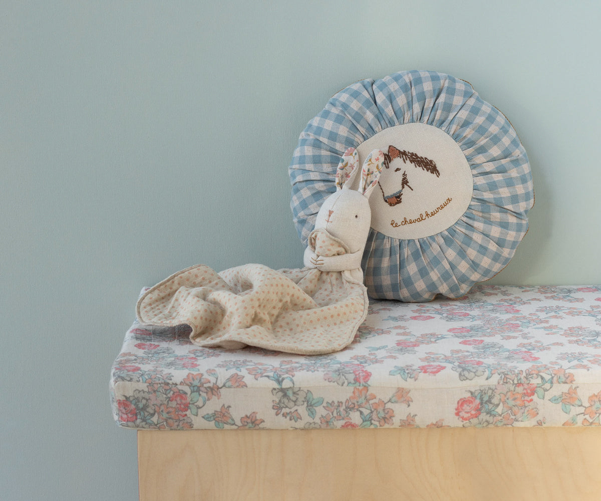 Stuffed animal toy and decorative pillow on a floral bench against a light blue wall