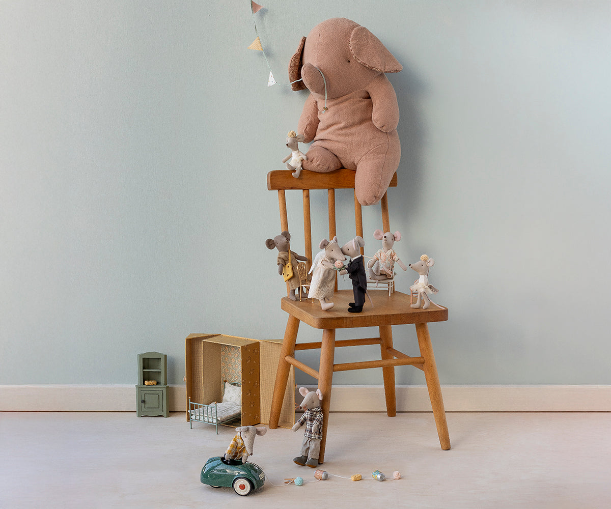 Children's toys including a plush elephant and teddy bears on a wooden stool against a light blue wall.