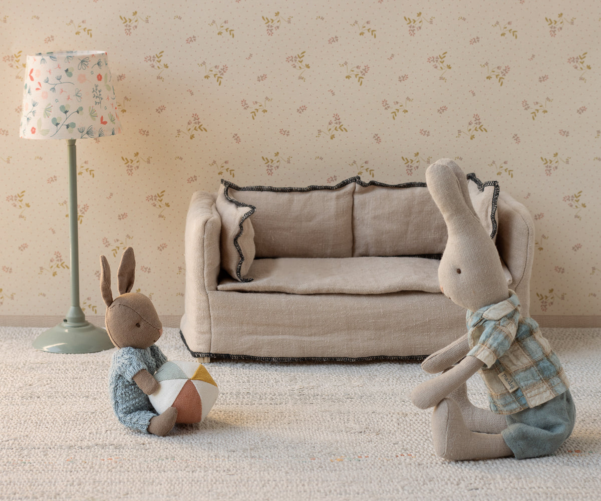 Two stuffed rabbits in a room with a sofa and lamp.