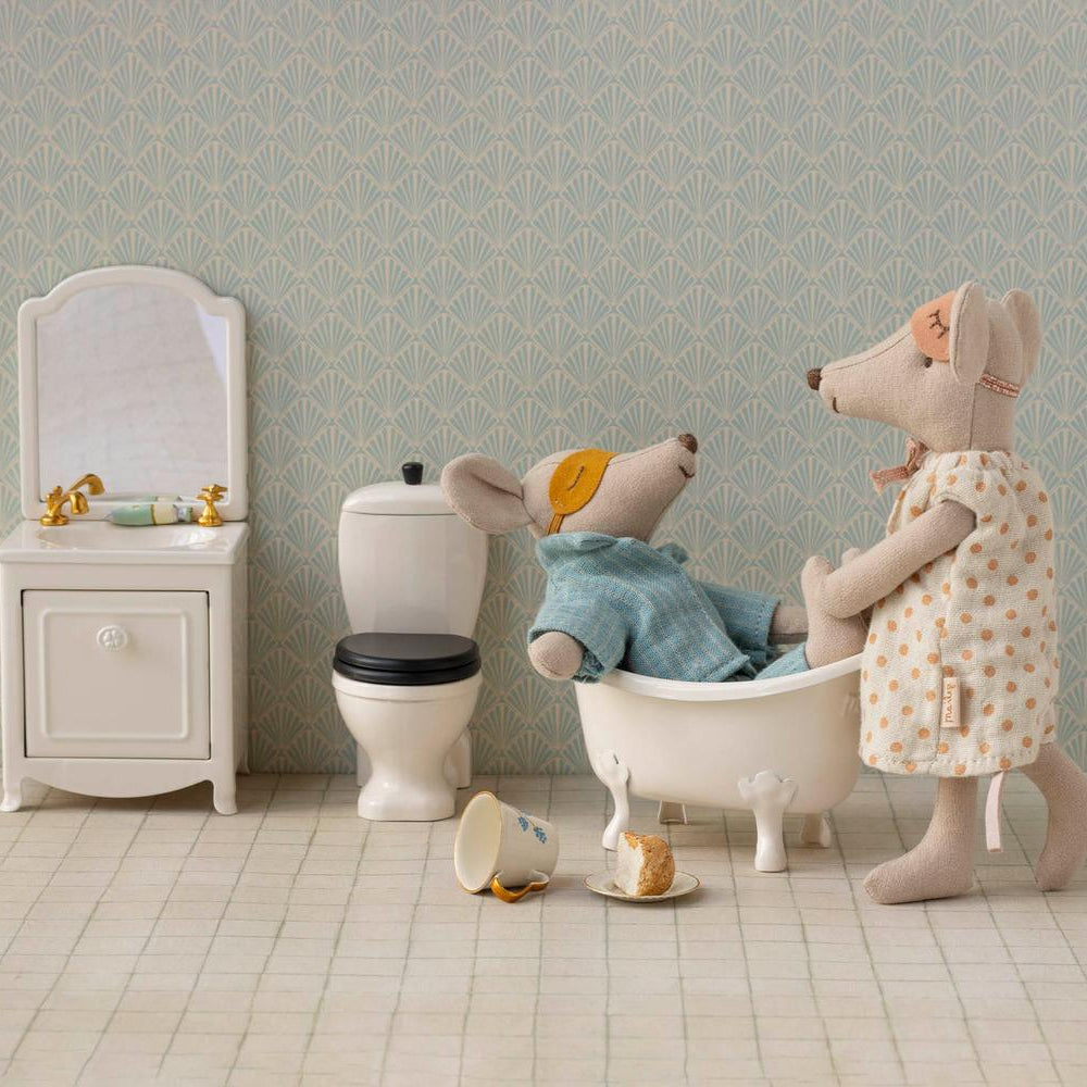 Maileg Mum mouse standing beside a miniature bathtub where Dad mouse sits inside, set in a dollhouse bathroom with a small toilet, sink, and tiled floor.