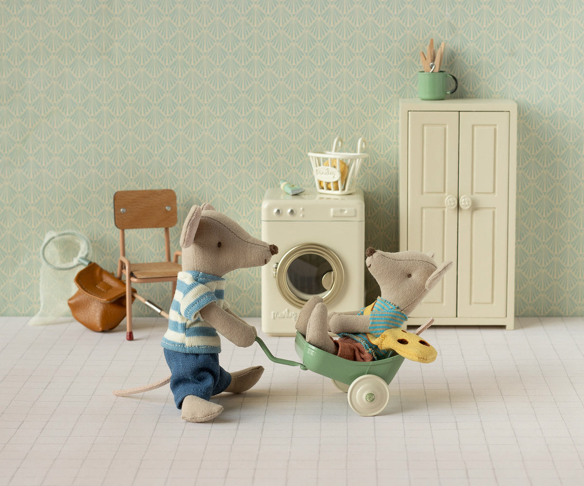 Two toy mice in a miniature room with a washing machine and furniture.