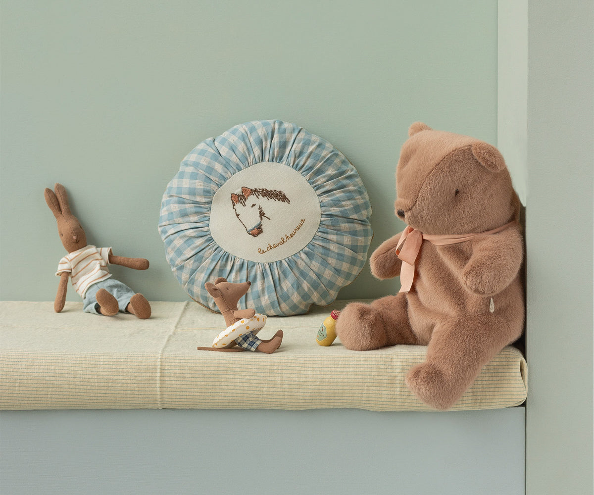 Stuffed teddy bear and rabbit on a shelf with decorative pillow against a light green wall
