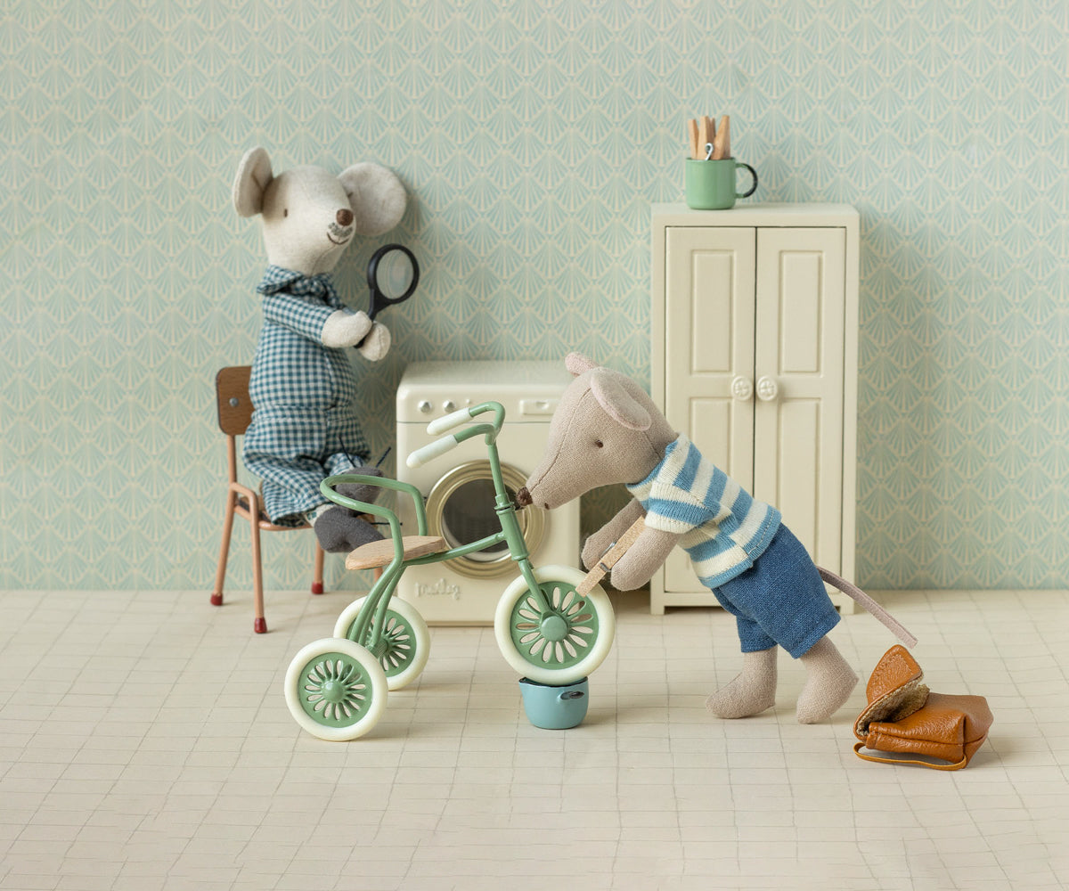 Two toy mice with a tricycle and other items in a room with light blue walls and a white floor.