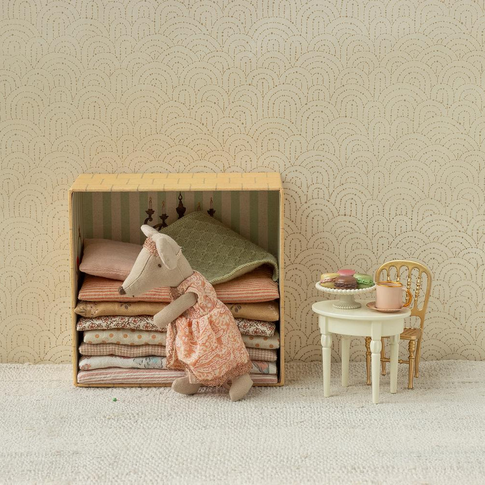 A Maileg toy set featuring a Big Sister mouse standing next to a wooden bed frame piled high with colorful layered mattresses, with a miniature table and chair set nearby holding tiny treats and a teapot.