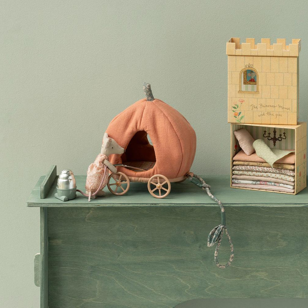 A Maileg toy set featuring an orange pumpkin carriage with a mouse beside it, placed next to an open illustrated castle box that reveals a stack of layered colorful mattresses and pillows on a bed frame.