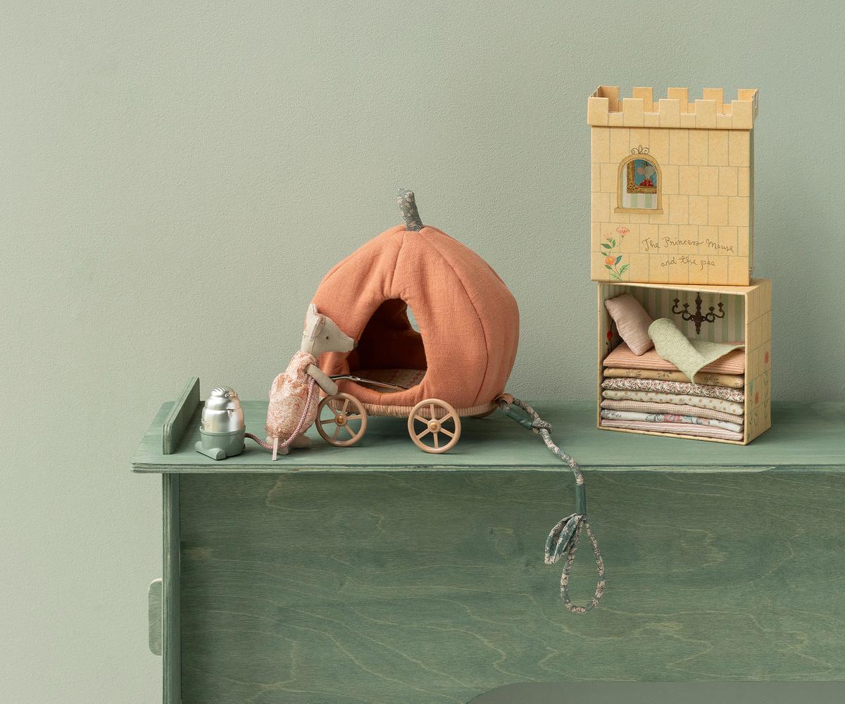 A Maileg toy set featuring an orange pumpkin carriage with a mouse beside it, placed next to an open illustrated castle box that reveals a stack of layered colorful mattresses and pillows on a bed frame.
