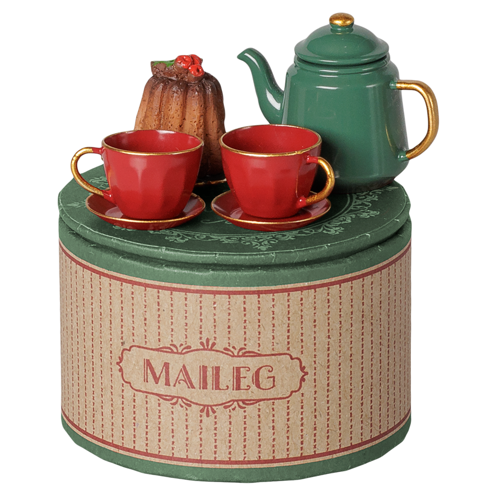 A Maileg Christmas tea party set featuring a round decorative gift tin, a green metal teapot with a gold knob and handle, two red teacups and saucers, and a miniature cake on a scalloped plate.