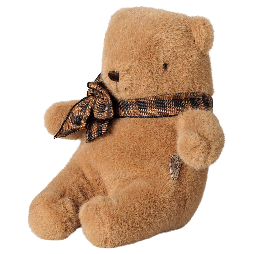 A brown Maileg mini teddy bear sitting with its legs extended forward, wearing a brown and black plaid bow around its neck.