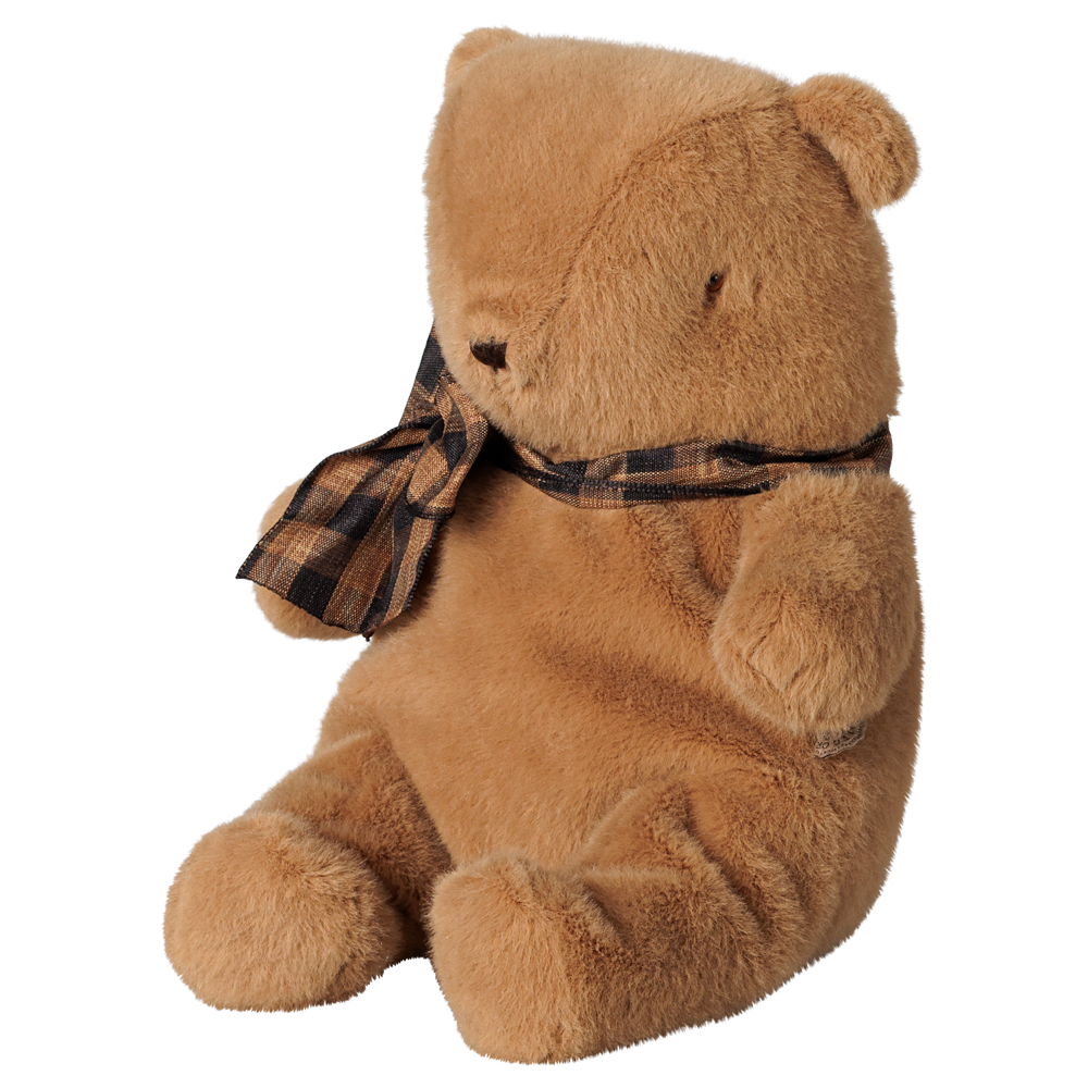 A small brown plush teddy bear by Maileg sitting upright against a transparent background, wearing a brown and black plaid bow around its neck.