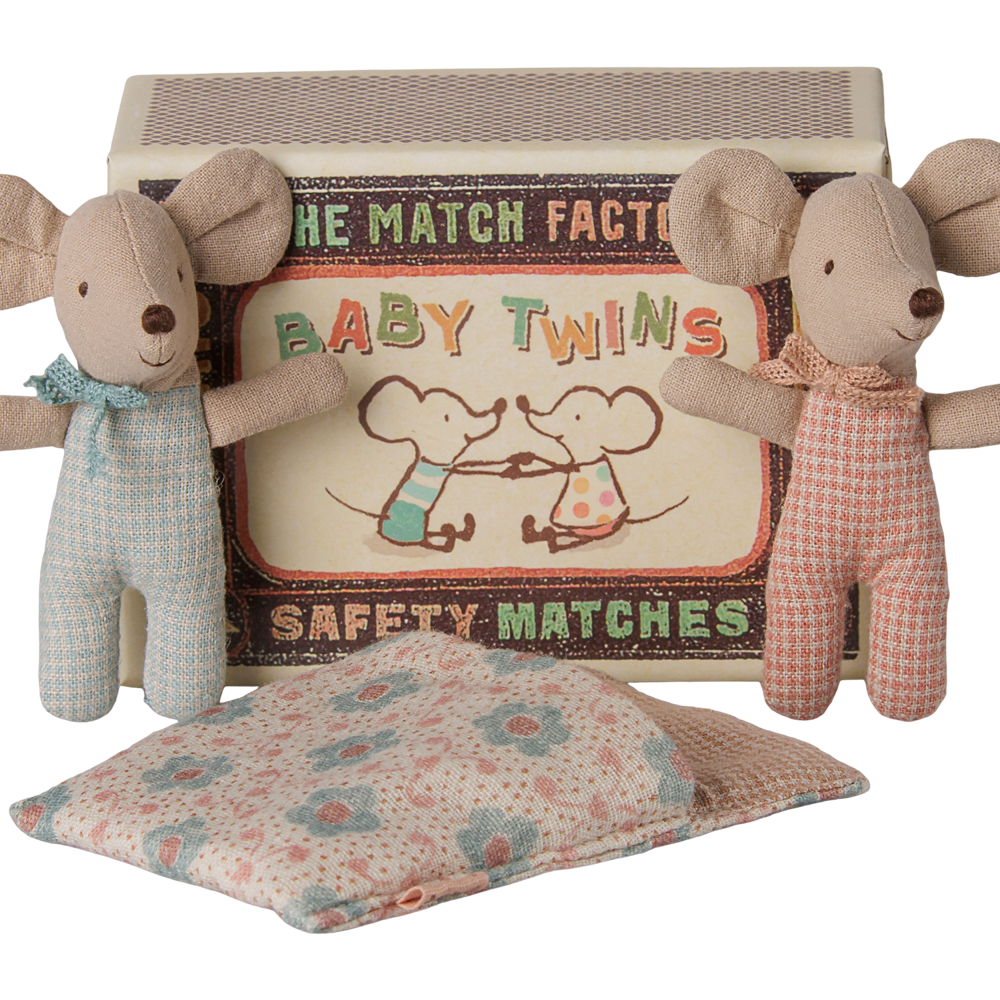 Two Maileg baby mice toys standing upright on either side of an open matchbox labeled "Baby Twins Safety Matches," with a patterned quilted sleeping bag resting in front.