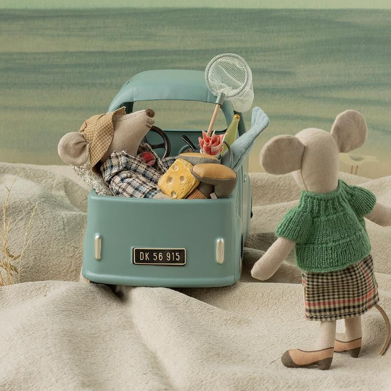 Grandma Mouse by Maileg stands on a sandy beach looking toward a mint-green toy car packed with other mice and accessories.