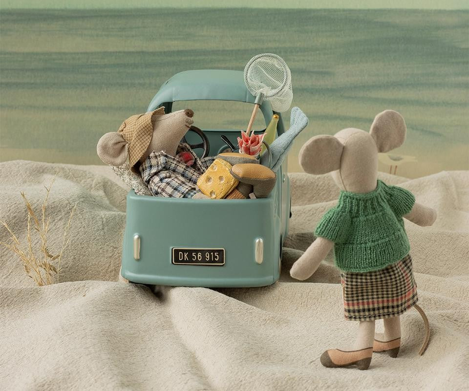 Grandma Mouse by Maileg stands on a sandy beach looking toward a mint-green toy car packed with other mice and accessories.