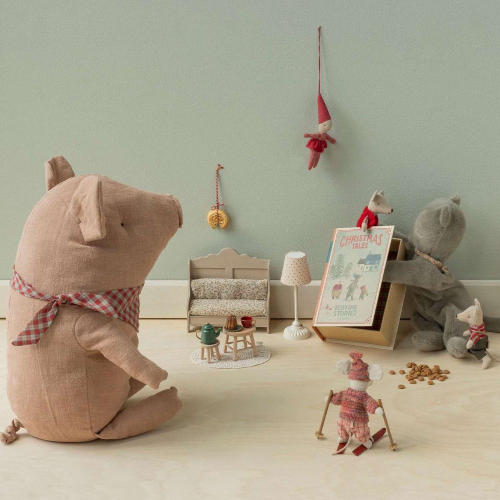 A miniature dollhouse scene featuring a large fabric pig toy, a grey stuffed mouse, and small Christmas-themed Maileg toys including a tea party set and tiny mice characters arranged in a cozy room.