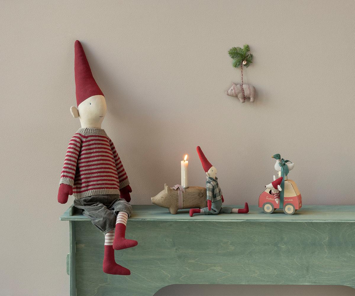 A festive holiday display featuring a large Maileg mouse doll in a red and white striped sweater and a tall pixy hat seated on a mint green ledge, with smaller Maileg mice, a miniature car-shaped box, and a toy pig figurine arranged nearby in front of a warm-toned background.