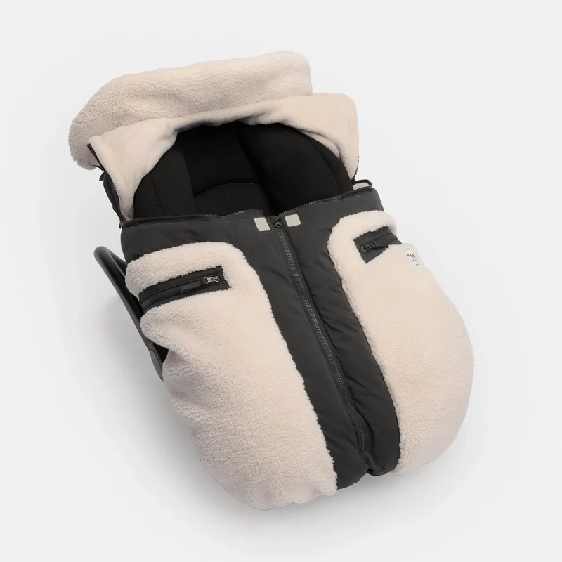 A baby footmuff in a warm cream fleece with black quilted panels and a black zipper, shown on a light gray background.