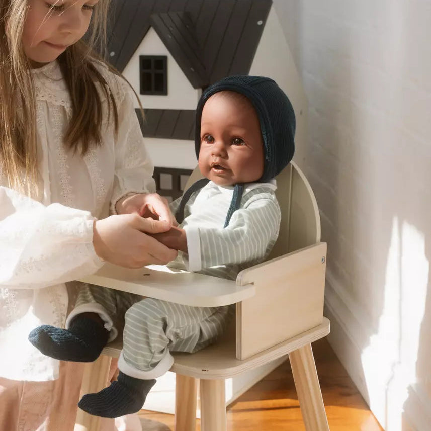 Two children playing with a baby doll in a room with a white wall and wooden floor.