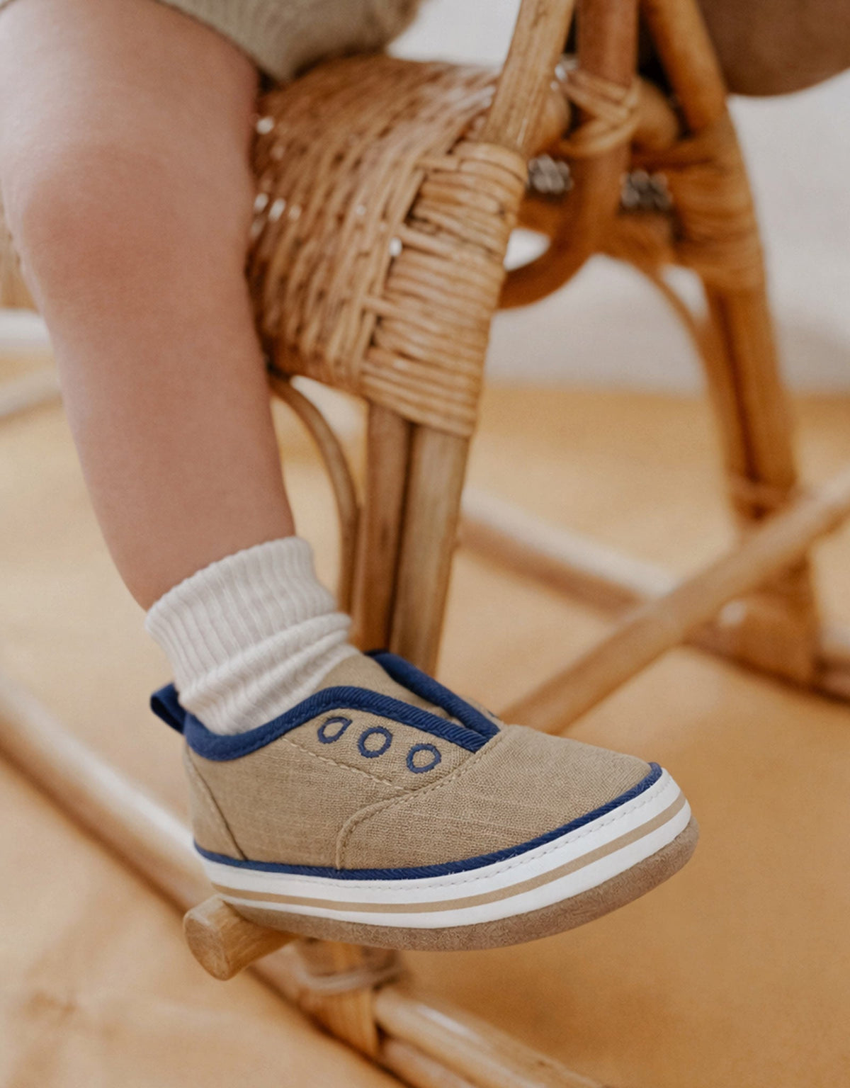 Child's foot wearing a tan shoe with blue accents on a wooden chair.