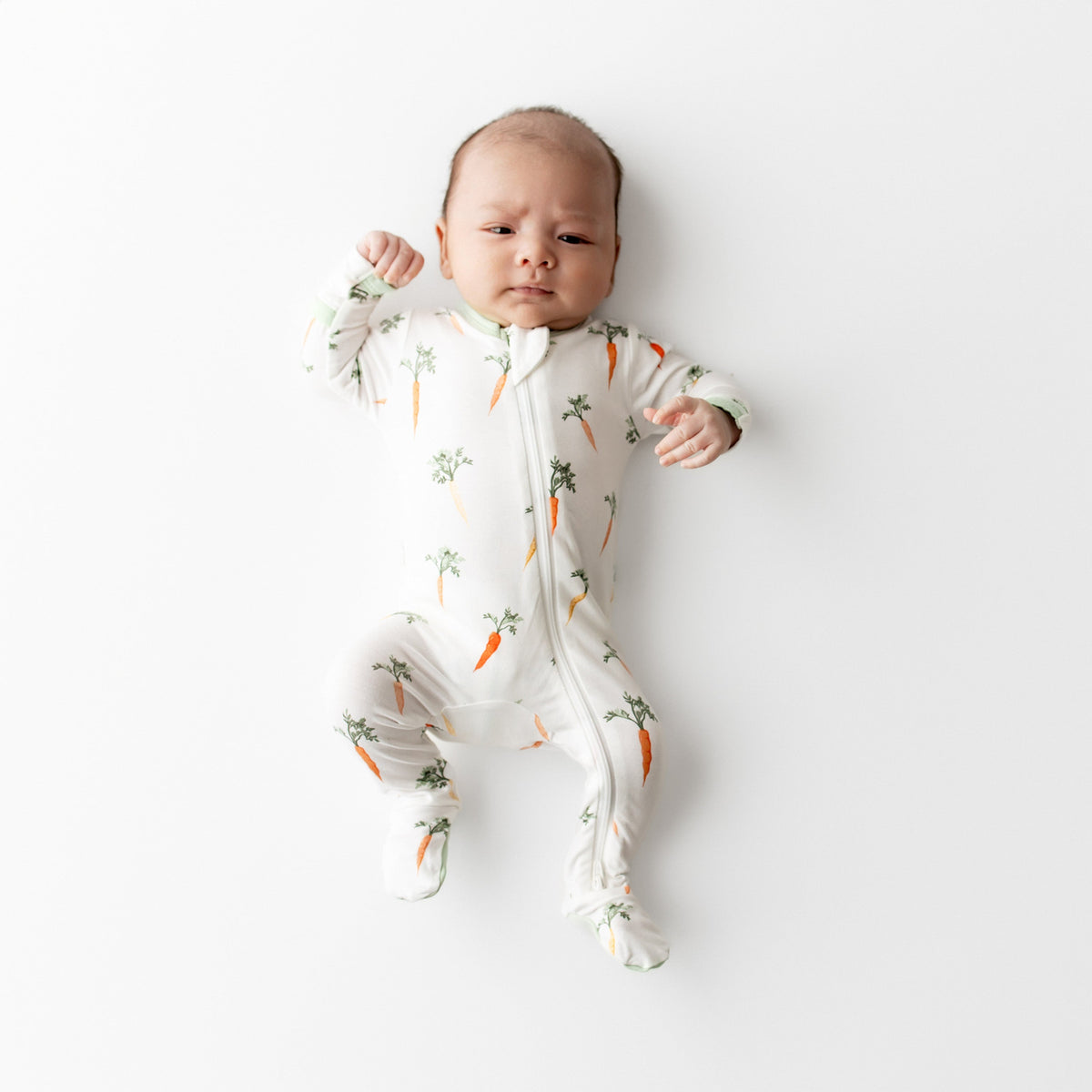 Baby wearing a white onesie with carrot pattern on a white background