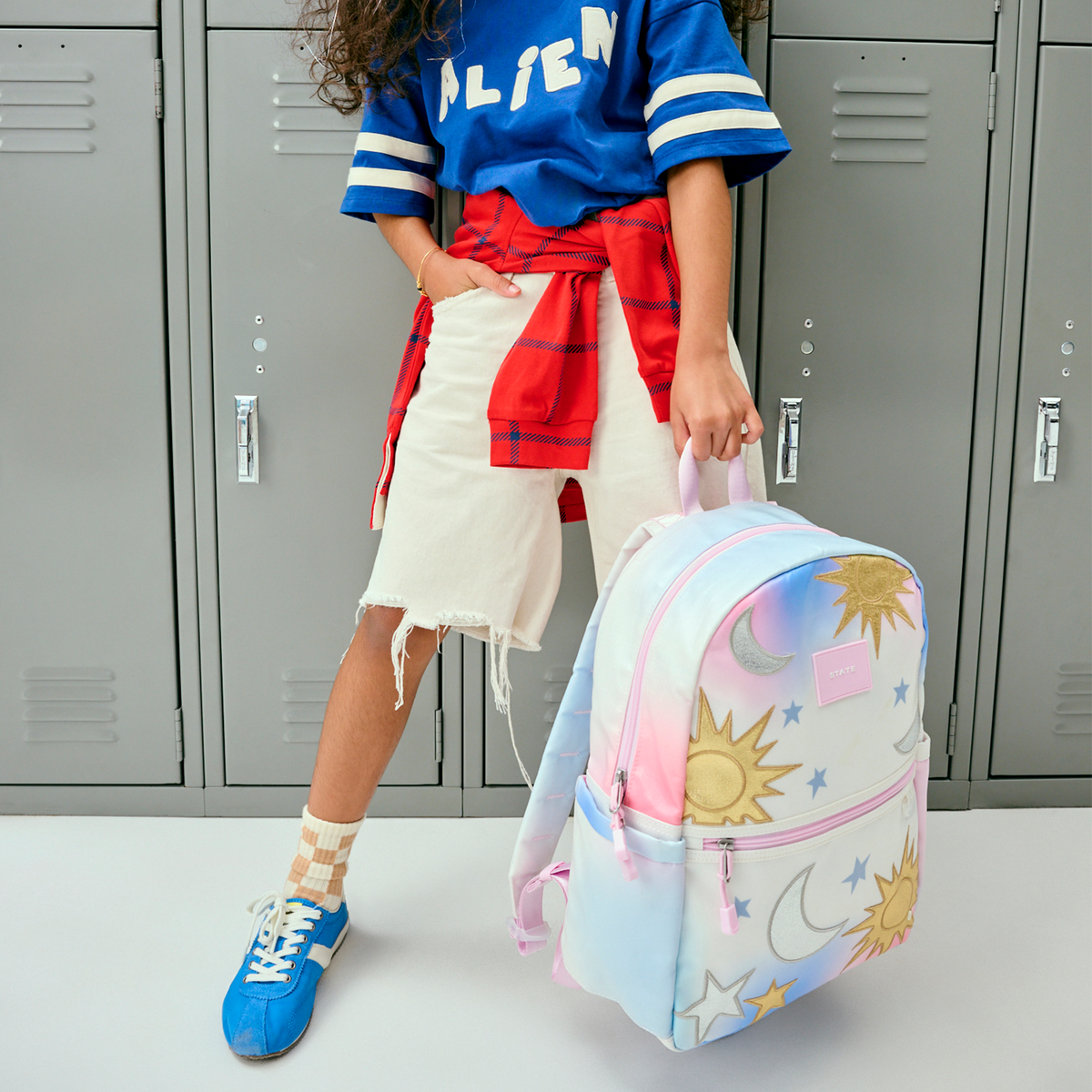 Person wearing a blue 'ALIEN' jersey with a colorful backpack in front of gray lockers.