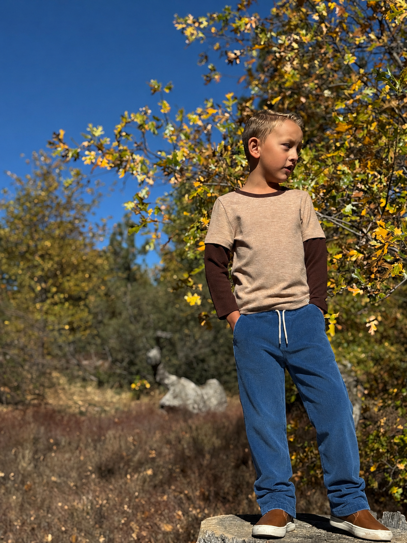 Young boy standing outdoors with trees and blue sky in the background