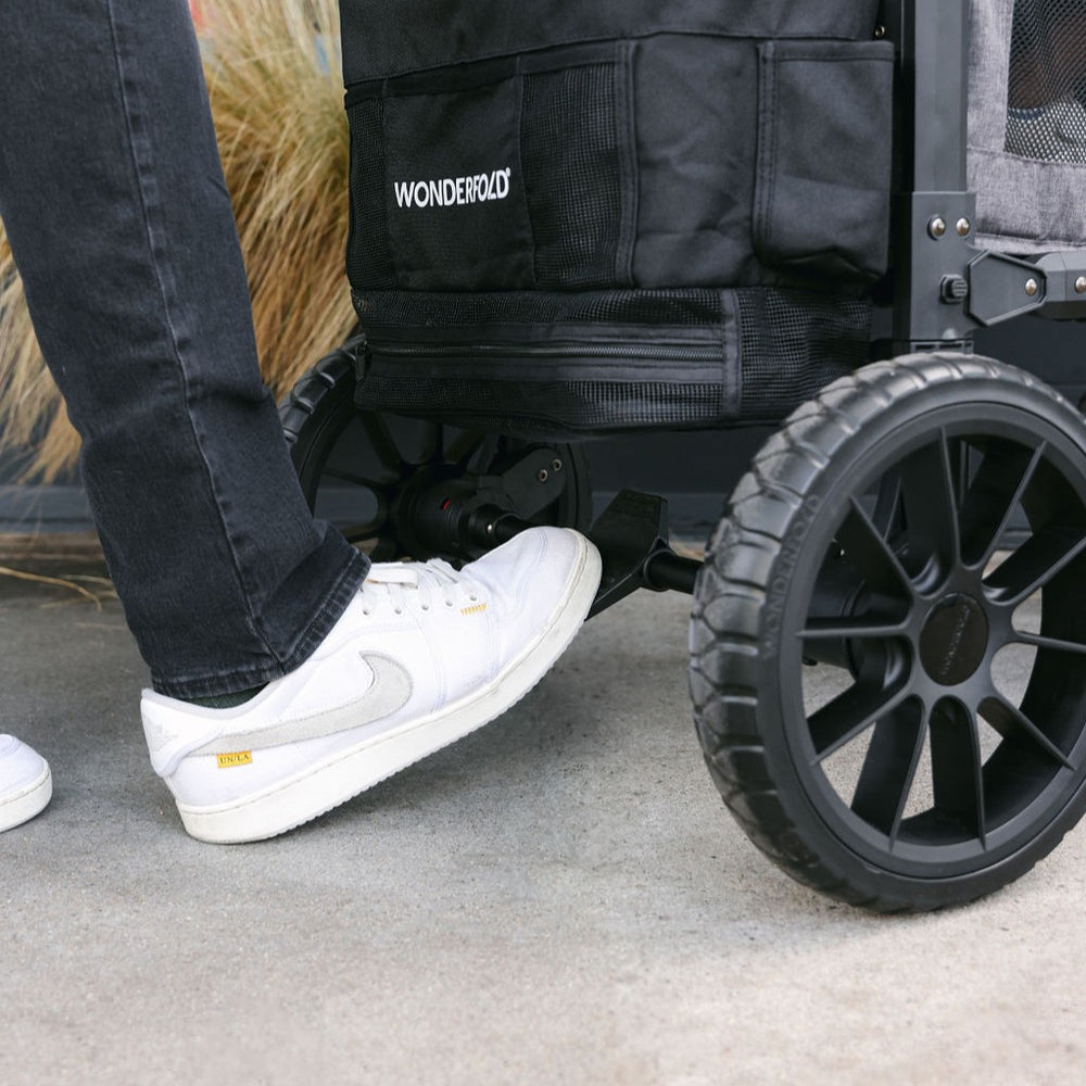 Person wearing white sneakers stepping onto a black WonderFold stroller.