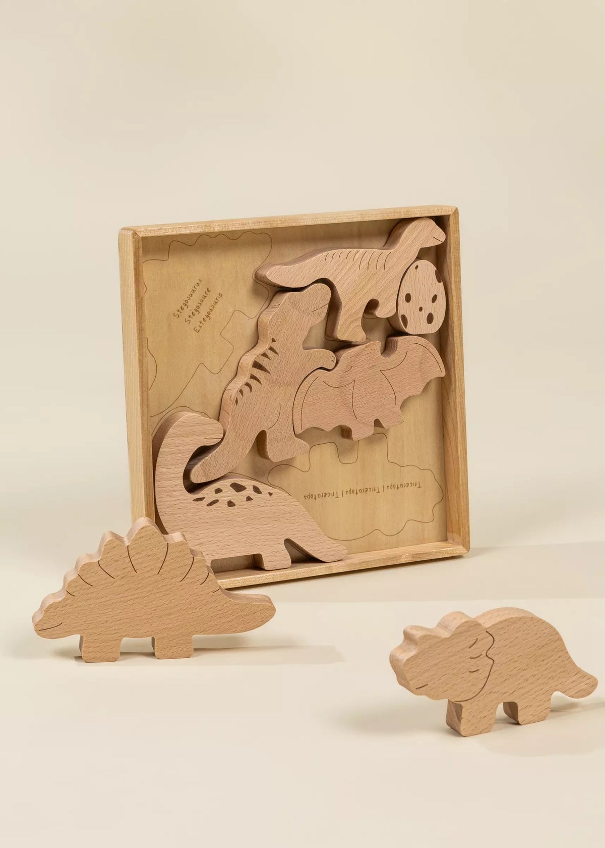 Set of wooden dinosaur toys with a box on a beige background