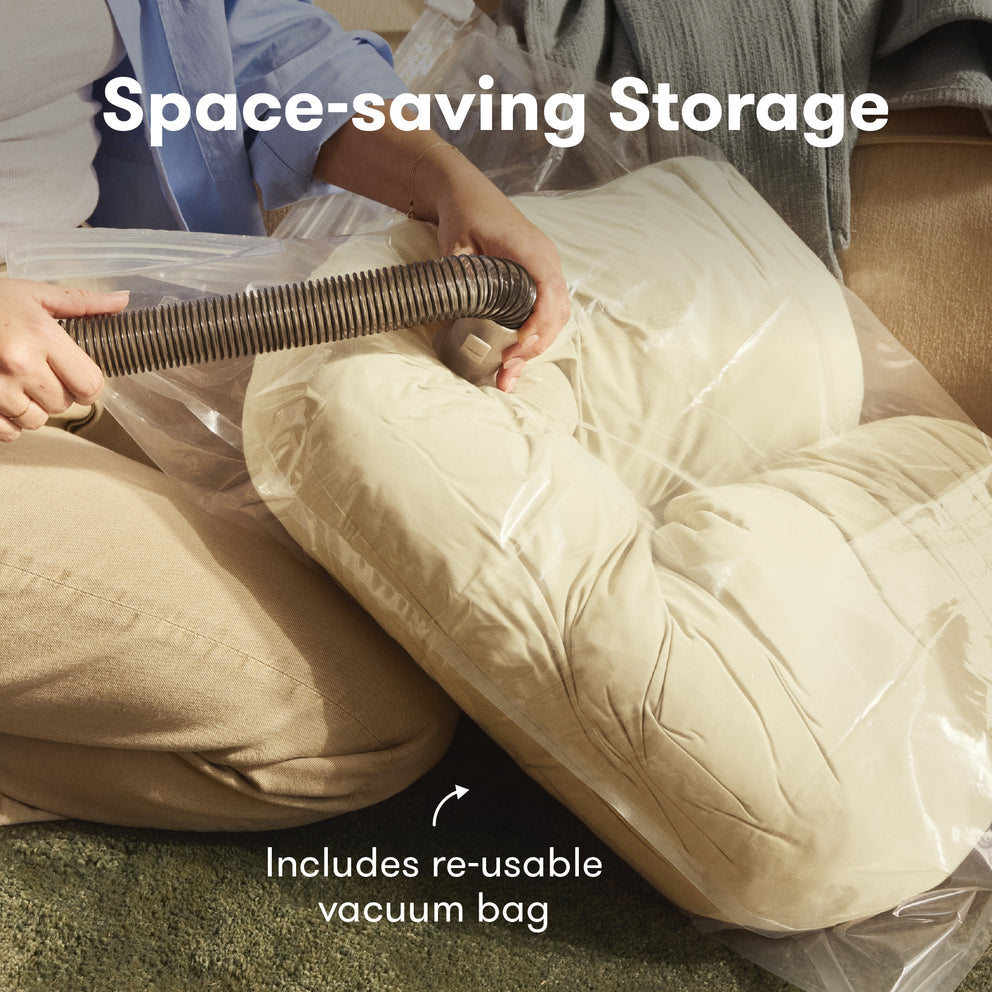 Person using a vacuum to compress a beige cushion into a clear vacuum bag with text 'Space-saving Storage' and 'Includes re-usable vacuum bag'.