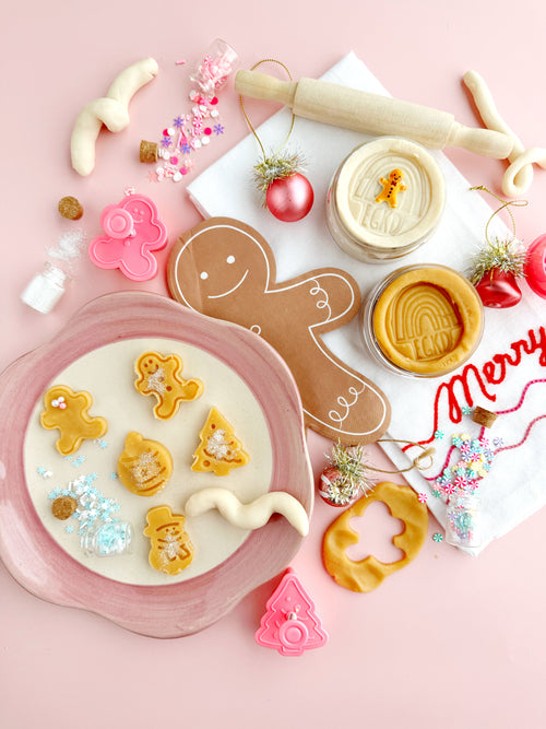Decorative cookies shaped like gingerbread men and trees on a pink surface with cookie cutters and festive decorations.