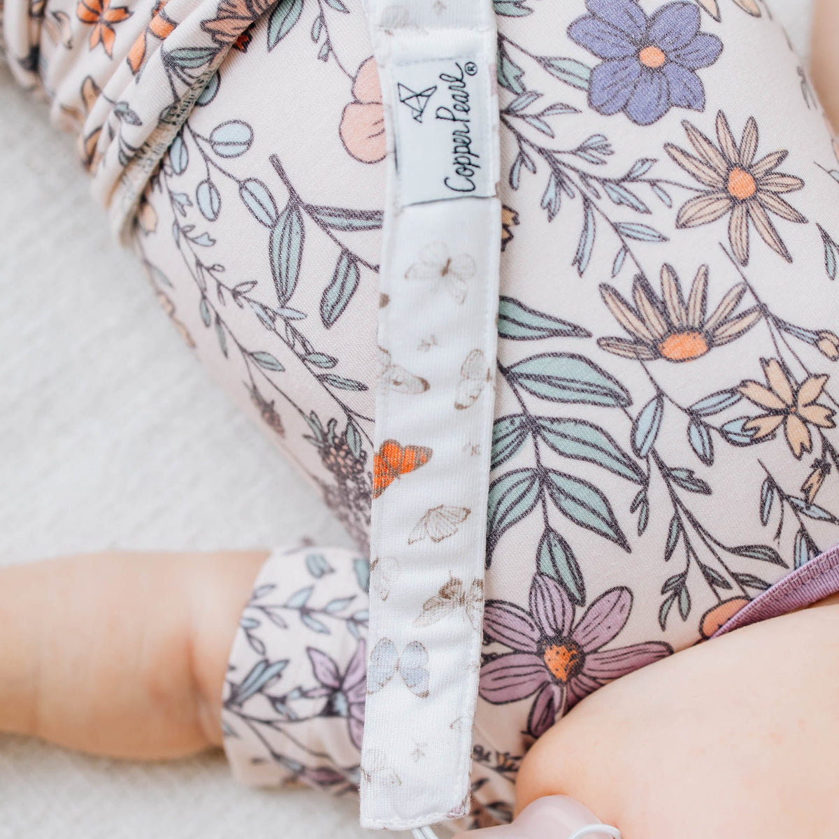 Floral-patterned baby romper with a visible brand label on a soft surface