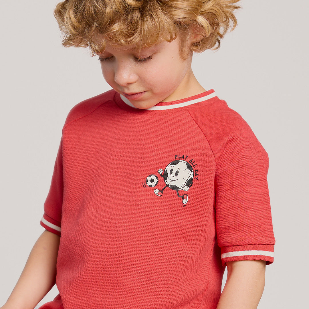 Child wearing a red shirt with a graphic design on a plain background