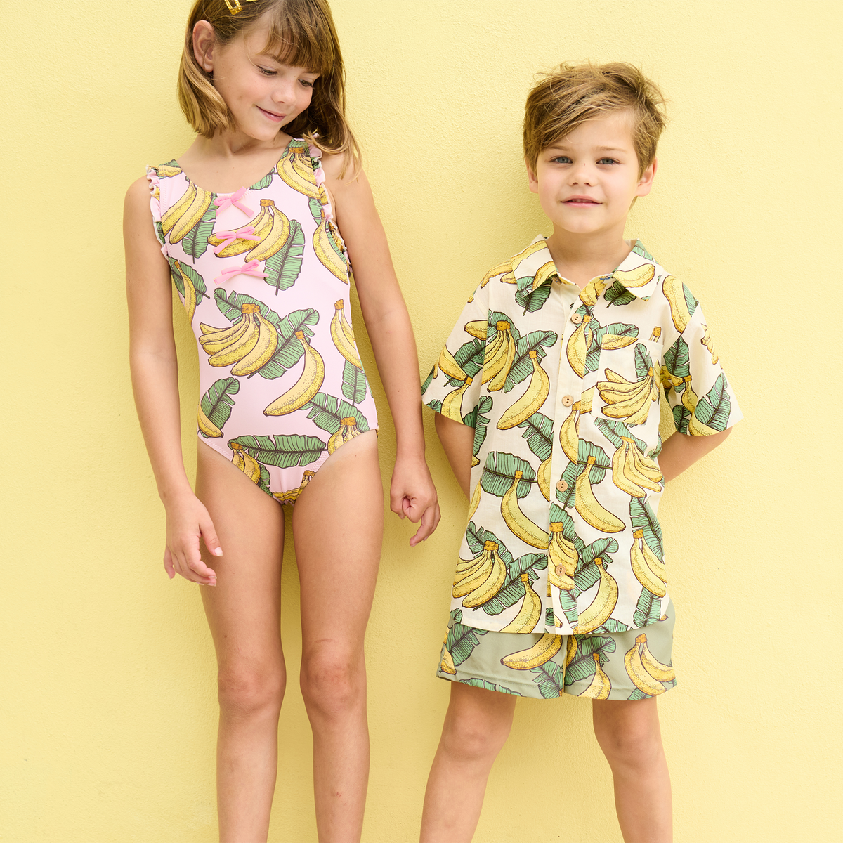 Two children wearing banana-patterned clothing on a yellow background