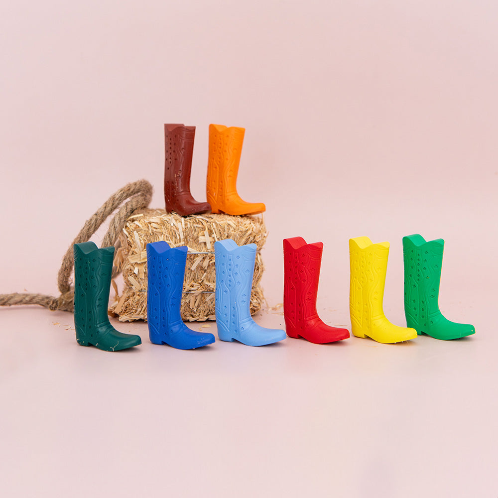 Colorful rubber boots arranged in a row with a straw bag on a light pink background