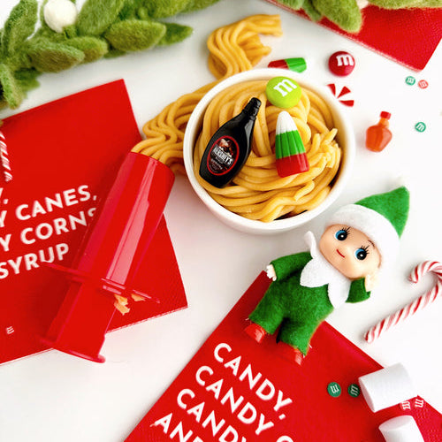 Christmas-themed setting with candy, elf figurine, and M&M's on a white surface.