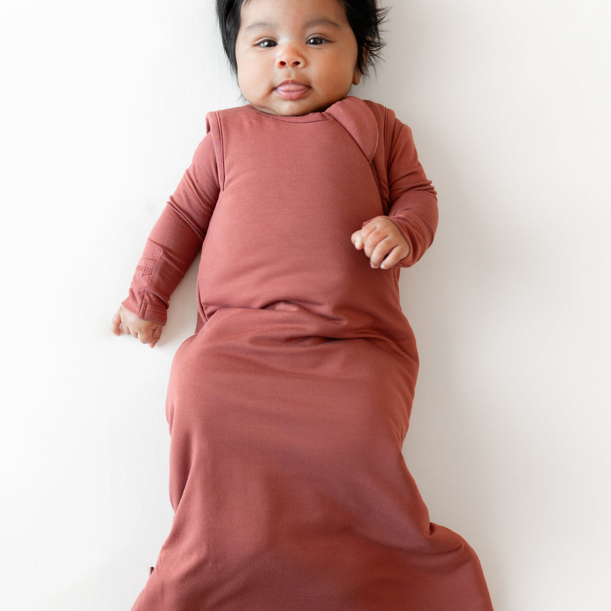 A baby lying on their back wearing a dusty rose long-sleeve swaddle blanket against a clean white background.