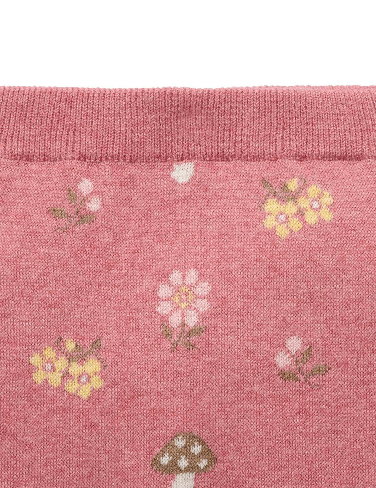 Close-up of a pink knit fabric with a repeating pattern of small flowers and mushrooms, showing a ribbed cuff at the top.