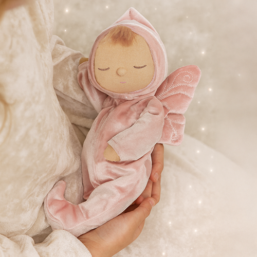 Pink plush baby toy held in a hand against a soft, neutral background