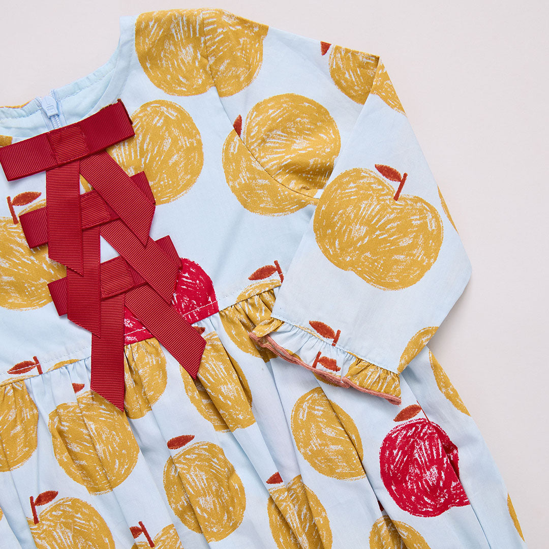 Children's dress with yellow apple pattern and red accents on a light blue background
