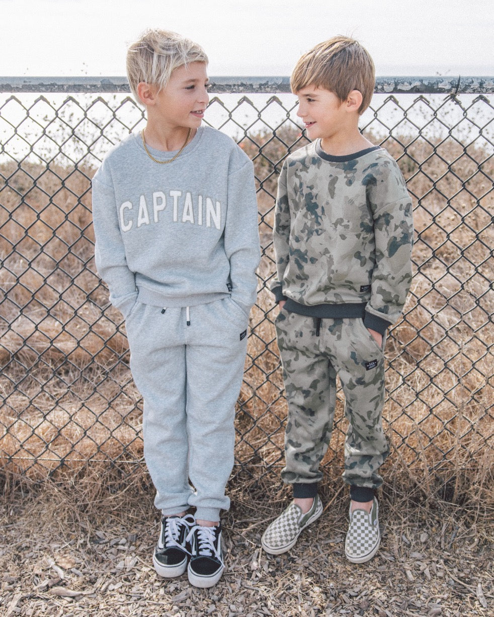 Two children wearing matching outfits in front of a chain-link fence.