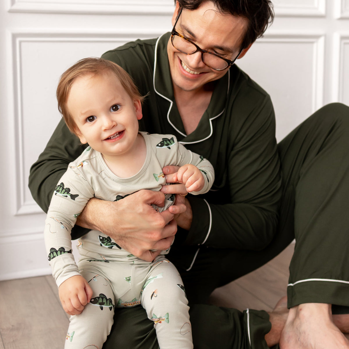 Man and child in matching pajamas sitting on a wooden floor.