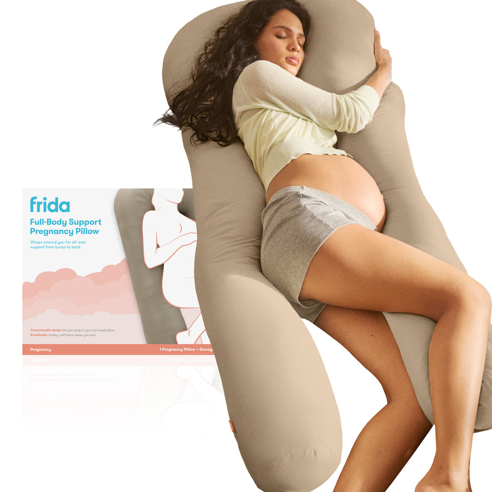Pregnant woman using a full-body support pregnancy pillow with 'frida' branding.
