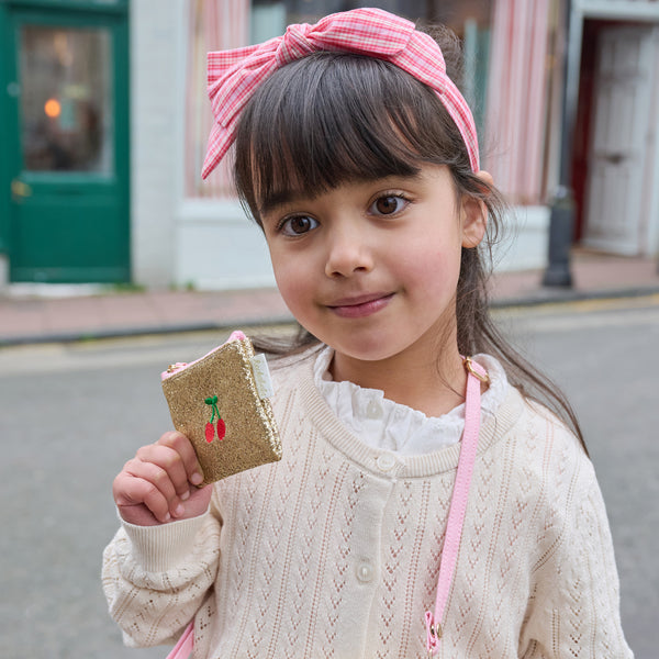 Young girl holding a small bag with a cherry design on a street.