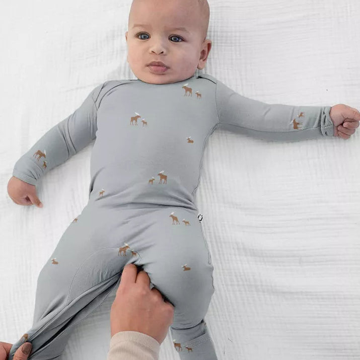 A baby wearing the günamüna Woof Sage Convertible Footie Pajama featuring an all-over small dog print.