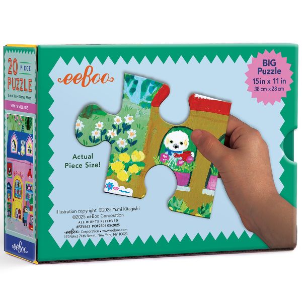 A hand holding a large, actual-size puzzle piece against the open 20 Piece Puzzle - Yumi's Village by Eeboo box, showcasing the vibrant green field and illustrated details.