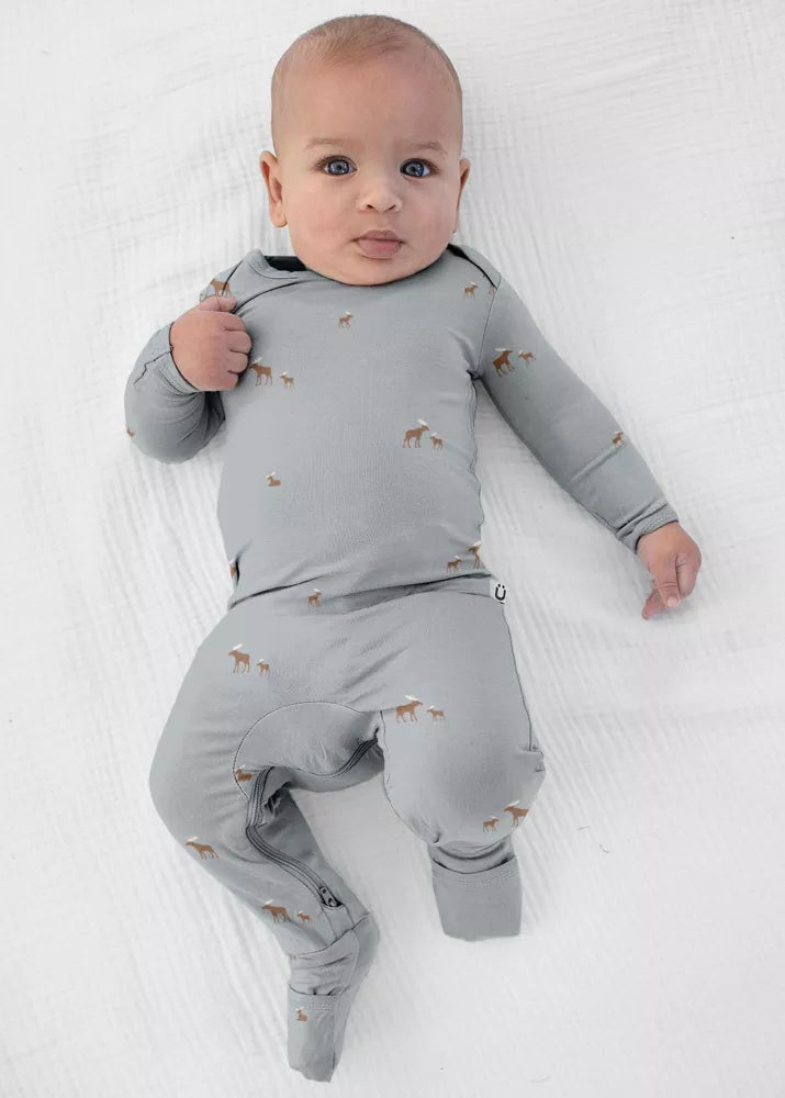 A baby wearing a sage grey günamüna Convertible Footie Pajama patterned with tiny dogs.